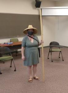 Five-foot tall woman standing in a classroom holding up a 2-meter tall stick