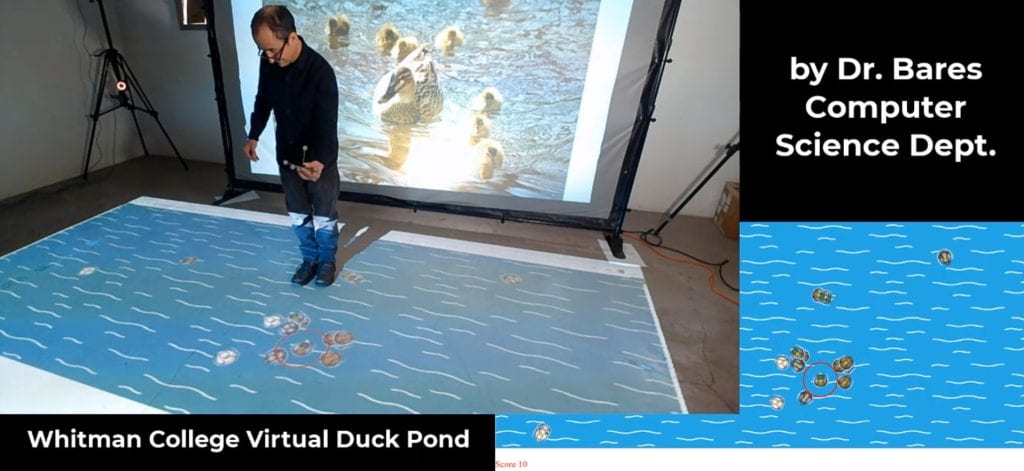William Bares holds a cluster of reflective markers to move a virtual duck. The image of the duck pond is projected onto the floor. Virtual ducks flock to follow the lead duck.