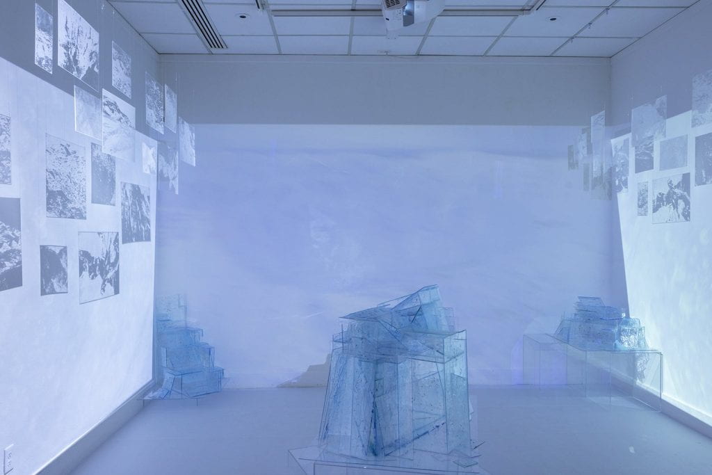 Projected imagery of an arctic scene from Greenland appears on the three walls. Plexiglass panels hang from the ceiling to catch projected light. Plexiglass ice sculptures are positioned about the space.