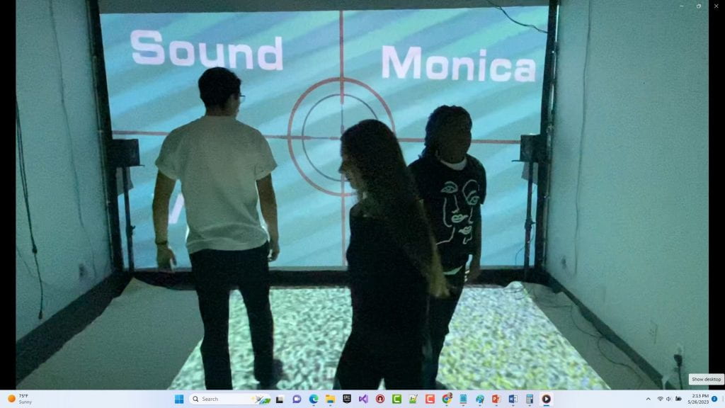 Three dance students stand over a floor-projected image of TV static. The back wall image projects a TV test pattern with the words Sound and Monica.